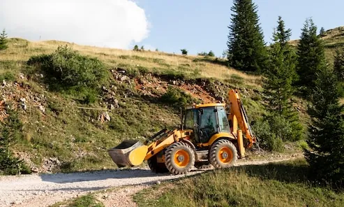 A yellow backhoe loader, with a bucket at the front and a digging arm at the back, on a dirt track